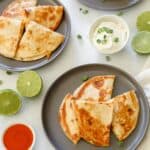 two quesadillas cut into fours with a side of sour cream, buffalo wing sauce, and limes