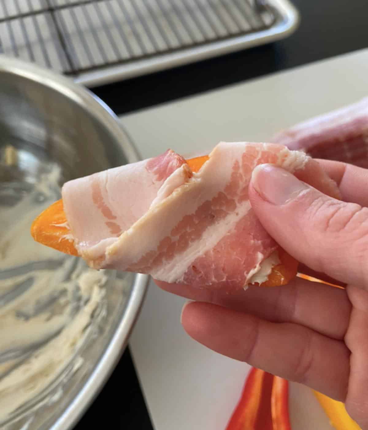 hand showing how to wrap bacon around pepper
