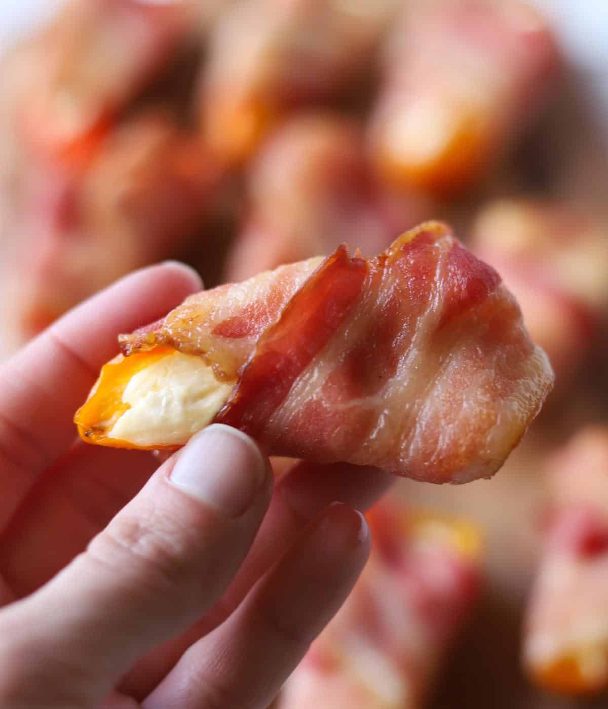 hand holding bacon wrapped stuffed pepper
