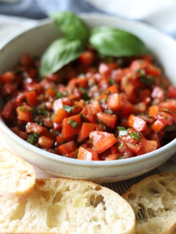 bruschetta in bowl topped with basil with slices of ciabatta sitting on side