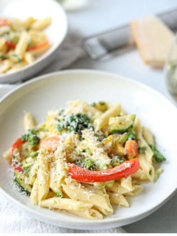Creamy vegetable pasta in a white bowl with parmesan cheese in background.