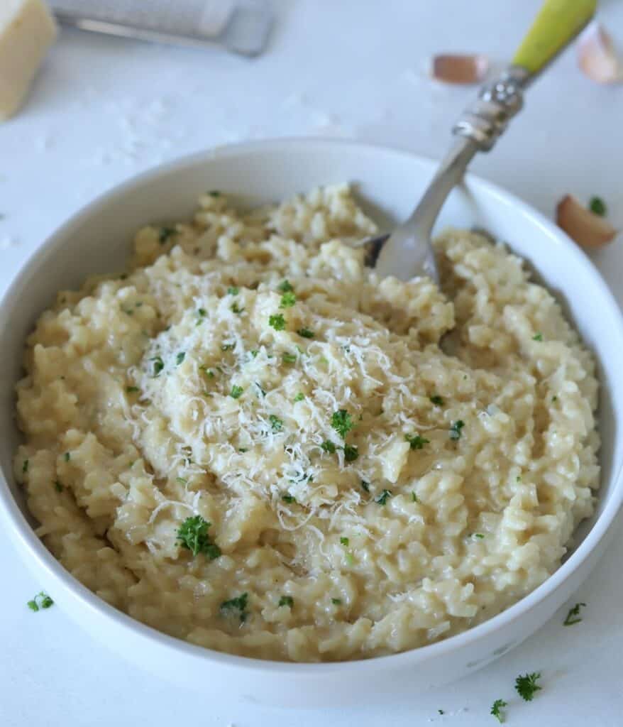 garlic parmesan risotto in white bowl with serving spoon