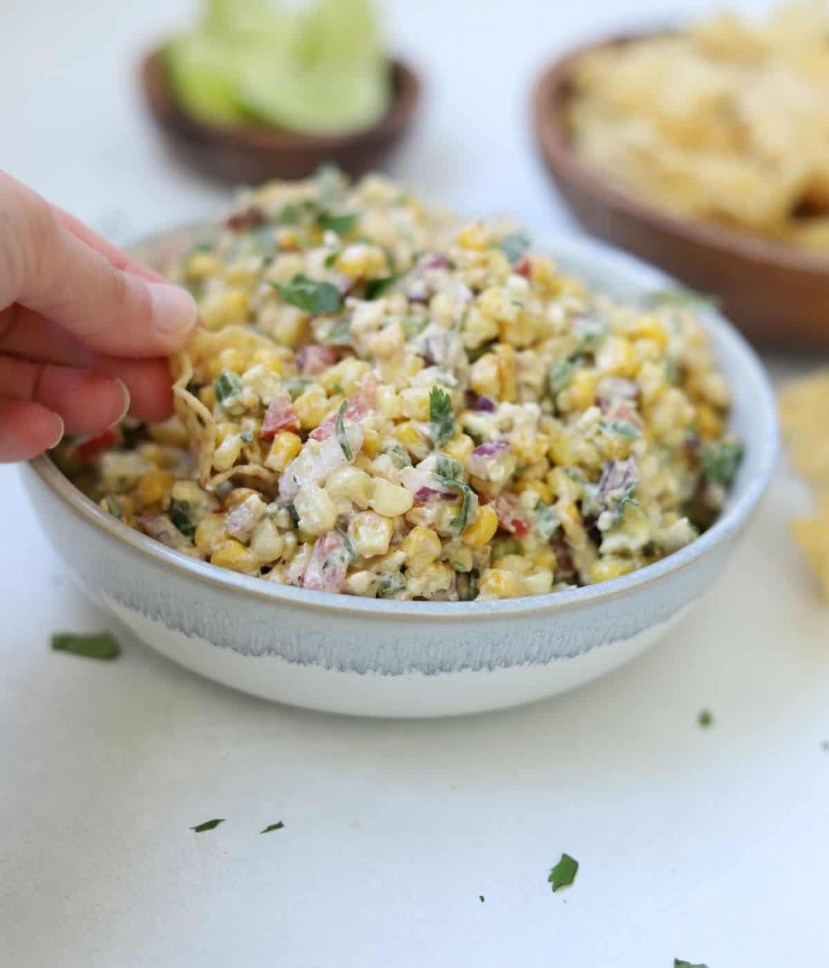 hand taking scoop out of corn dip with chip