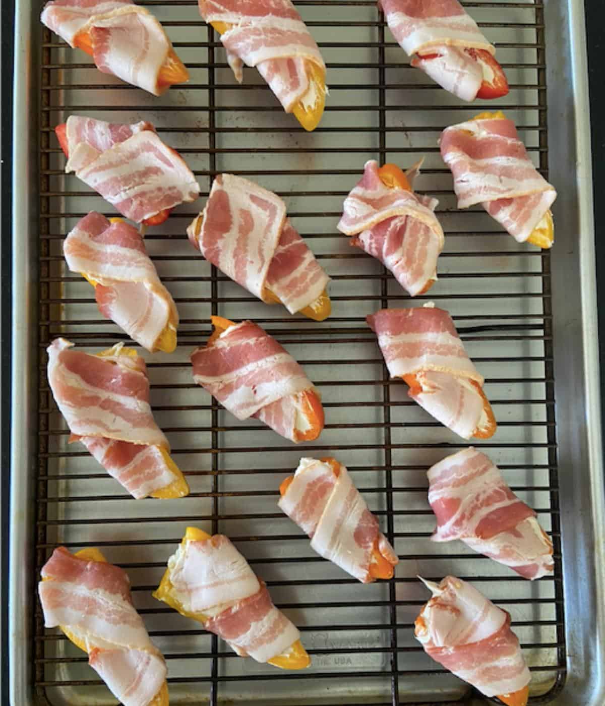 stuffed sweet peppers wrapped in bacon on baking rack on cookie sheet