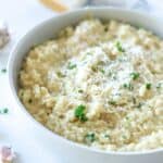 garlic parmesan risotto in white bowl topped with parmesan cheese and parsley