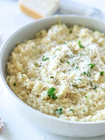 garlic parmesan risotto in white bowl topped with parmesan cheese and parsley