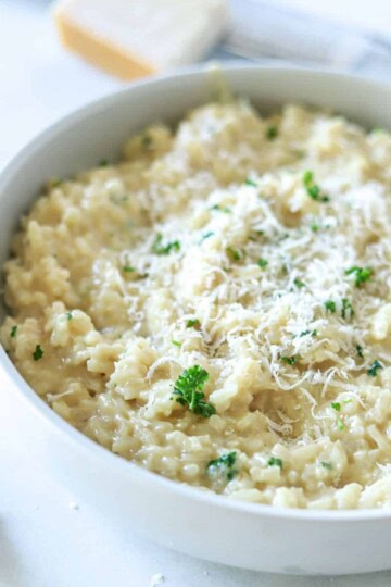 garlic parmesan risotto in white bowl topped with parmesan cheese and parsley