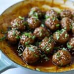 asian meatballs in enamel pan tossed in glaze with green onion and sesame seed