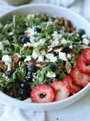 white bowl full of strawberry and pecan salad topped with feta