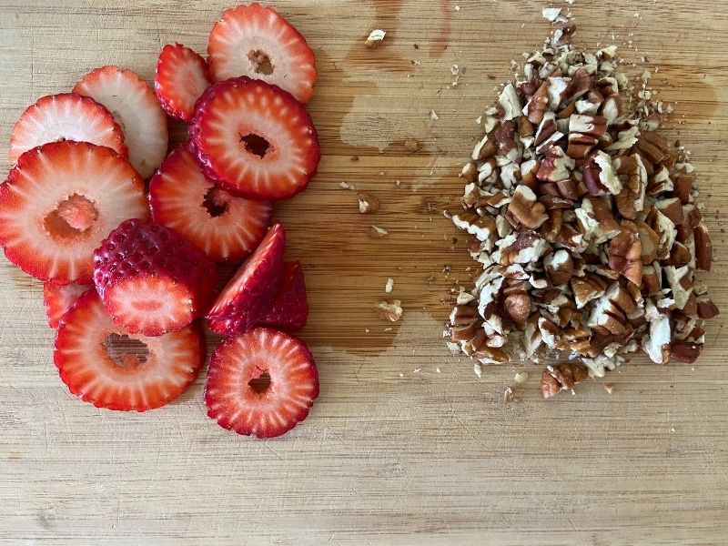 chopped strawberries and pecans on wooden cutting board