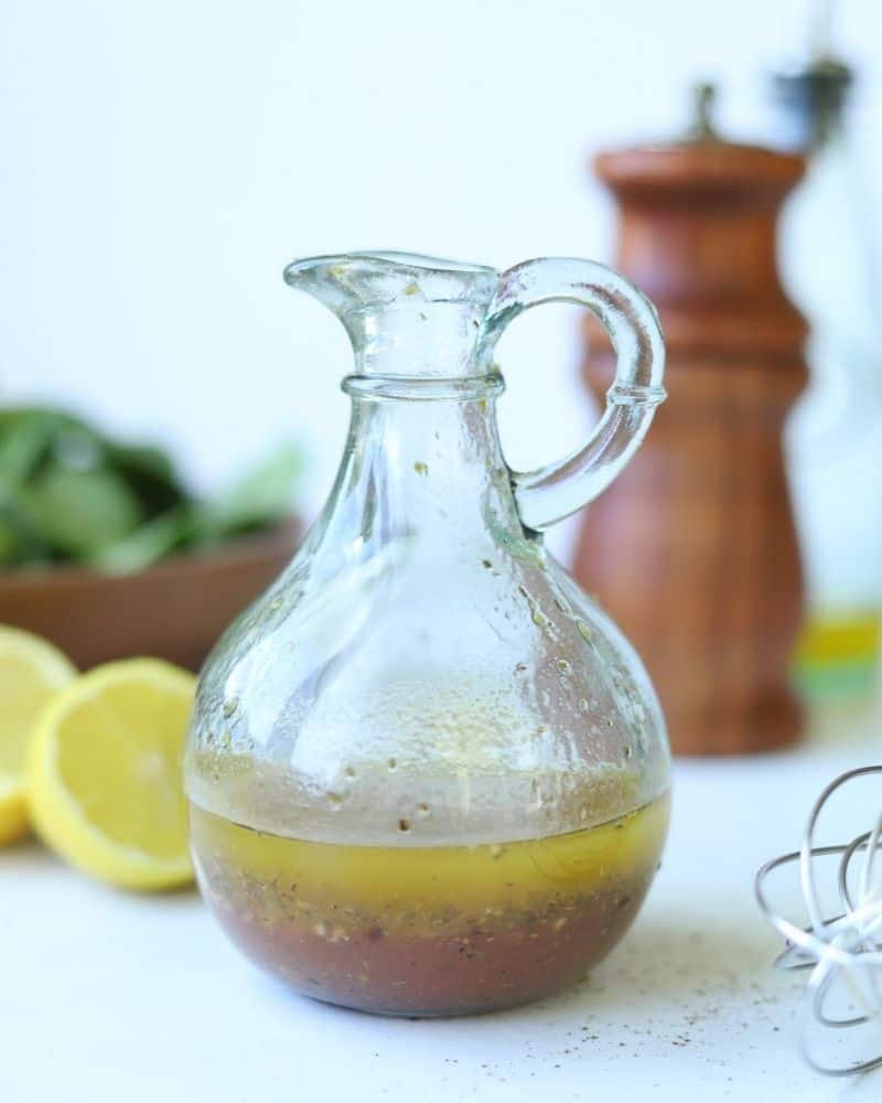 homemade lemon greek dressing in glass jar with lemons and spinach in background