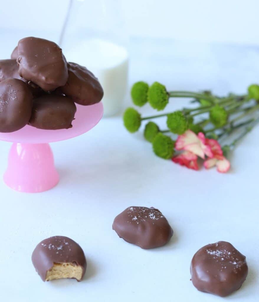 peanut butter eggs on pink stand with milk in a glass and flowers in background