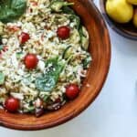 orzo greek pasta salad in large wooden bowl with lemons in another bowl