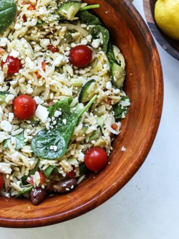 orzo greek pasta salad in large wooden bowl with lemons in another bowl