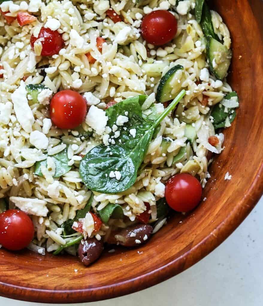 close up view of orzo greek pasta salad in wooden bowl
