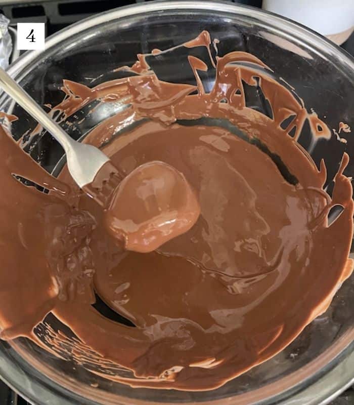 dipping peanut butter eggs into melting chocolate using a fork