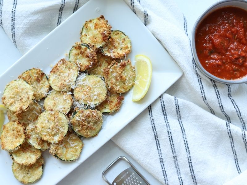 air fryer zucchini on white plate with a side of marinara