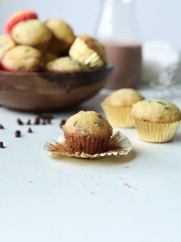 Mini chocolate chip muffin in front of bowl full of muffins and chocolate milk container