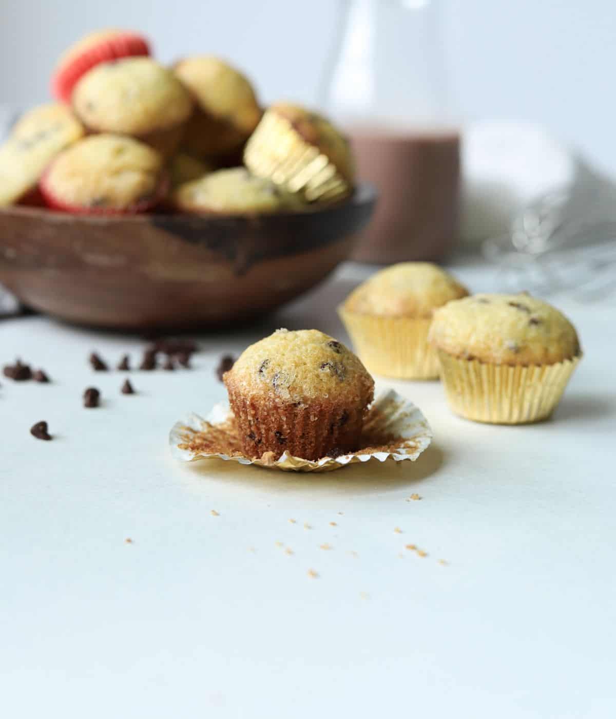 mini chocolate chip muffin in front of bowl full of muffins and chocolate milk container
