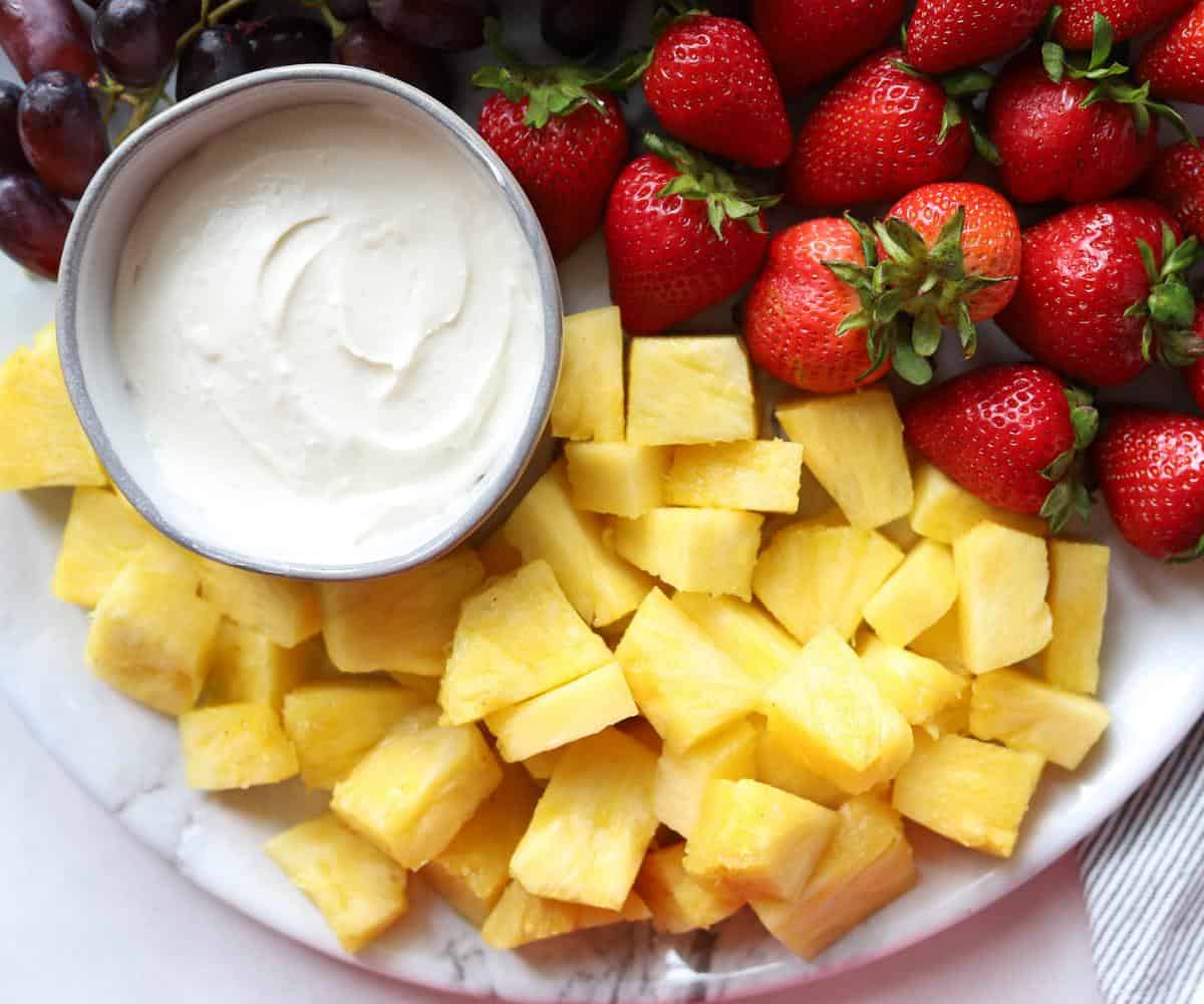 platter with strawberries and pineapple with a bowl full of fruit dip