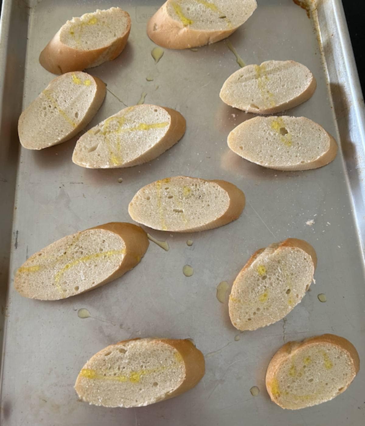 French bread sliced and ready to bake on cookie sheet.