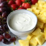 marshmallow fluff fruit dip in gray bowl with pineapple grapes and strawberries surrounding the dip