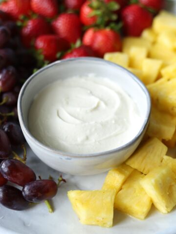 marshmallow fluff fruit dip in gray bowl with pineapple grapes and strawberries surrounding the dip