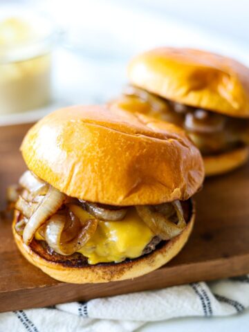 two smash burgers on a wooden platter with american cheese and sautéed onions