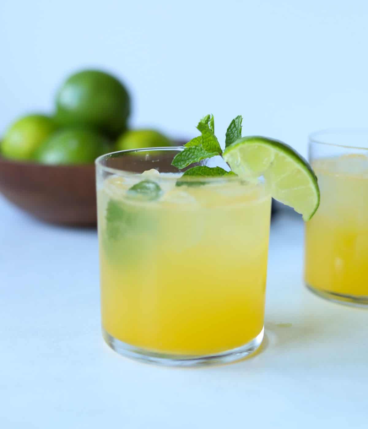 close up view of mango mojito cocktail glass with limes in background