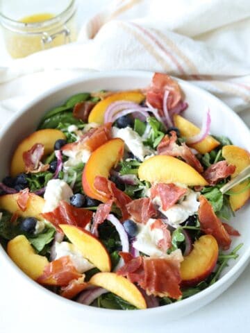 peach burrata salad in large white bowl with gold fork