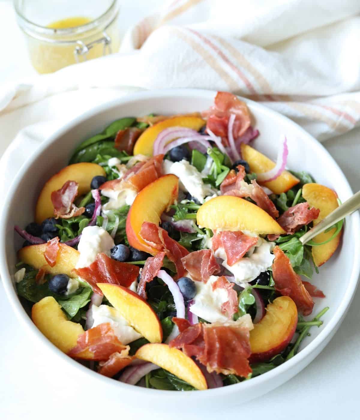 peach burrata salad in large white bowl with gold fork