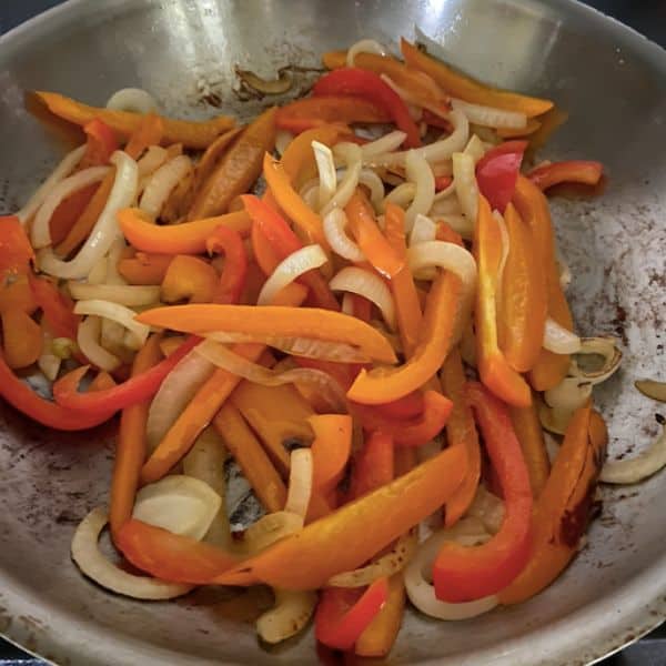 peppers and onions cooking in stainless skillet