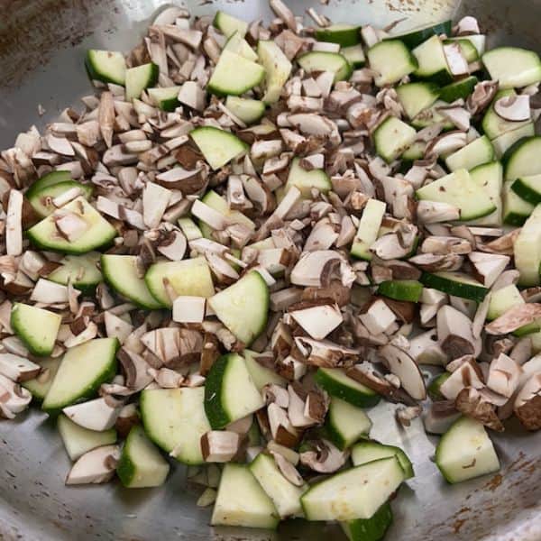 zucchini and mushrooms sautéing in stainless pan