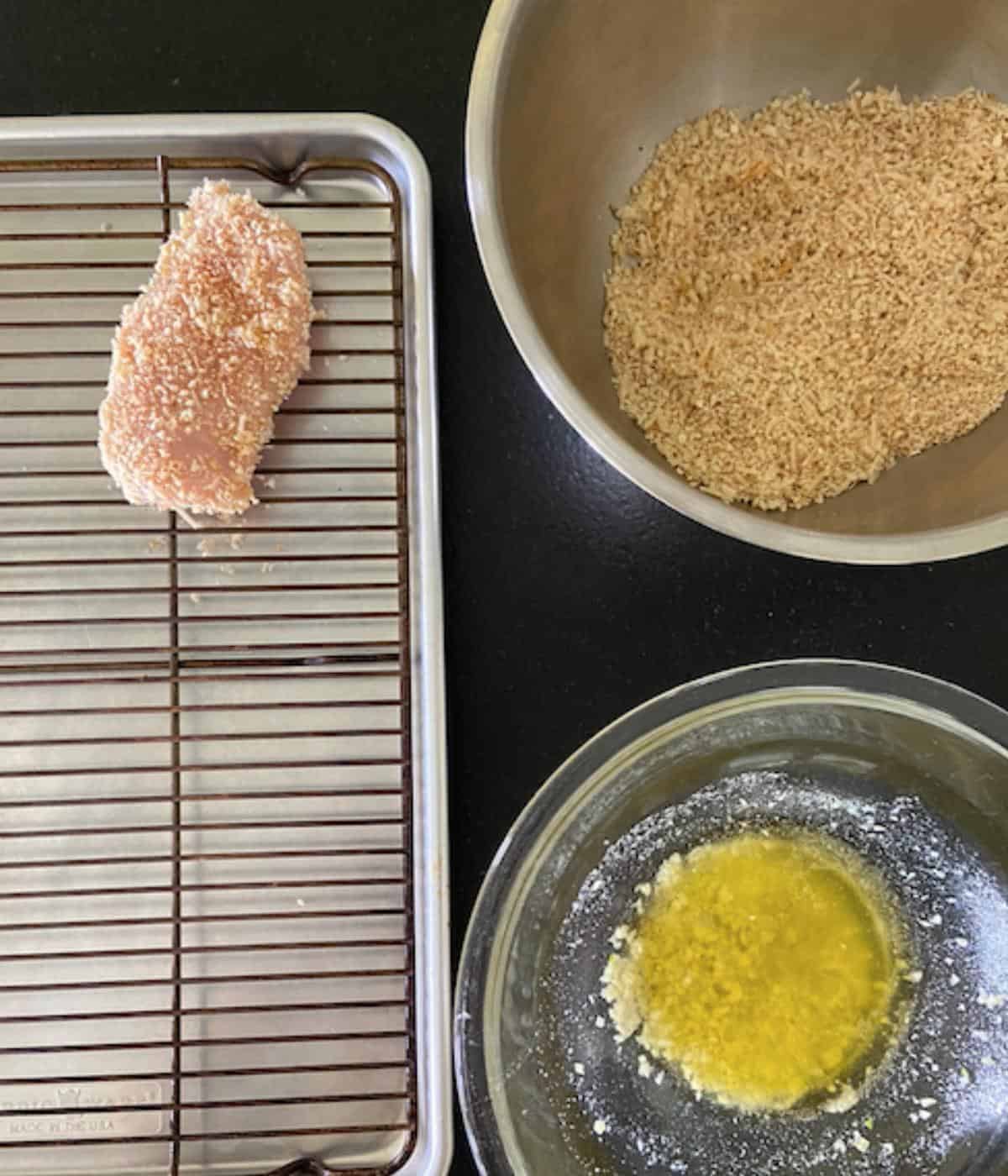 chicken breast on baking rack with bowl of garlic butter and bowl of breading mixture
