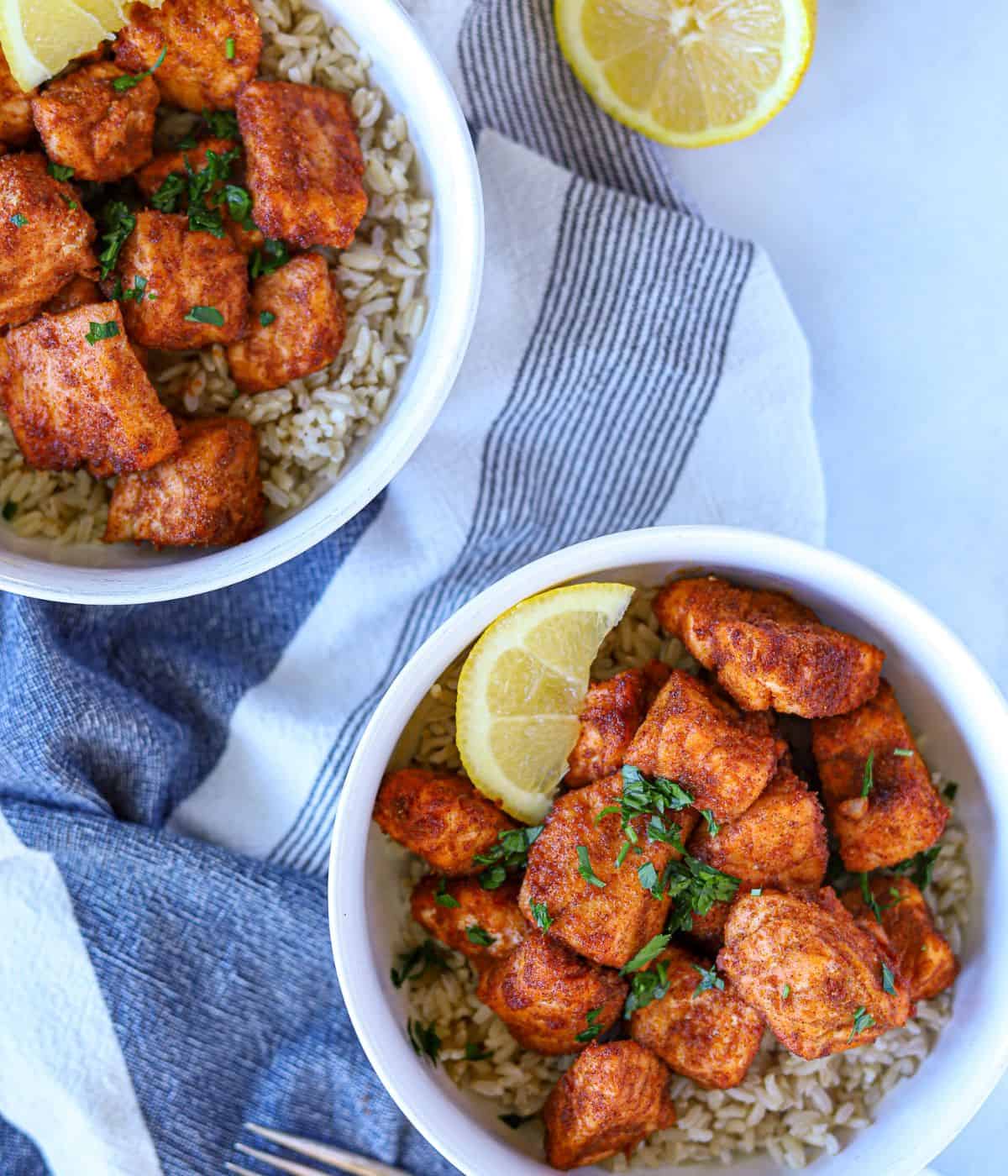 two bowls full of rice and topped with cajun salmon bites