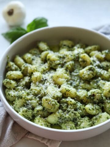 gnocchi in white serving bowl with basil and garlic in background