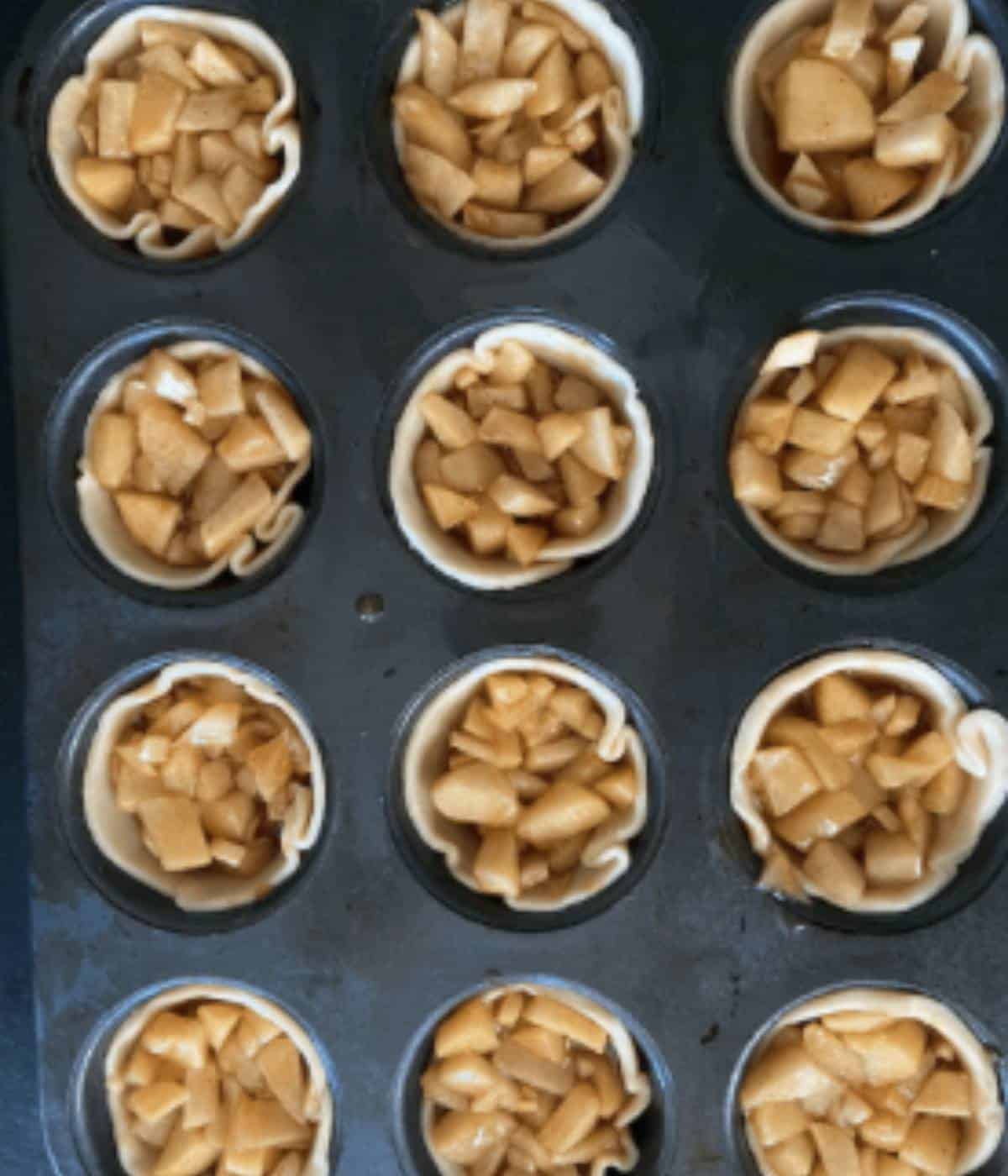 Mini apple pies in muffin tin ready for oven.