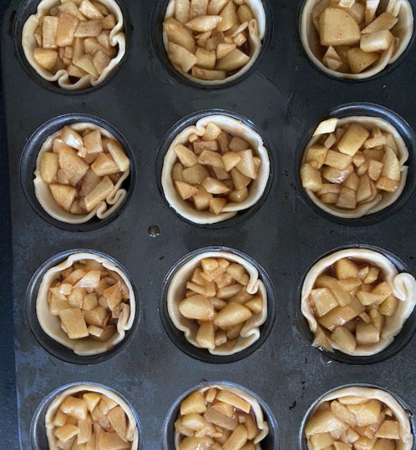 muffin tins filled with pie crust and filling ready to bake