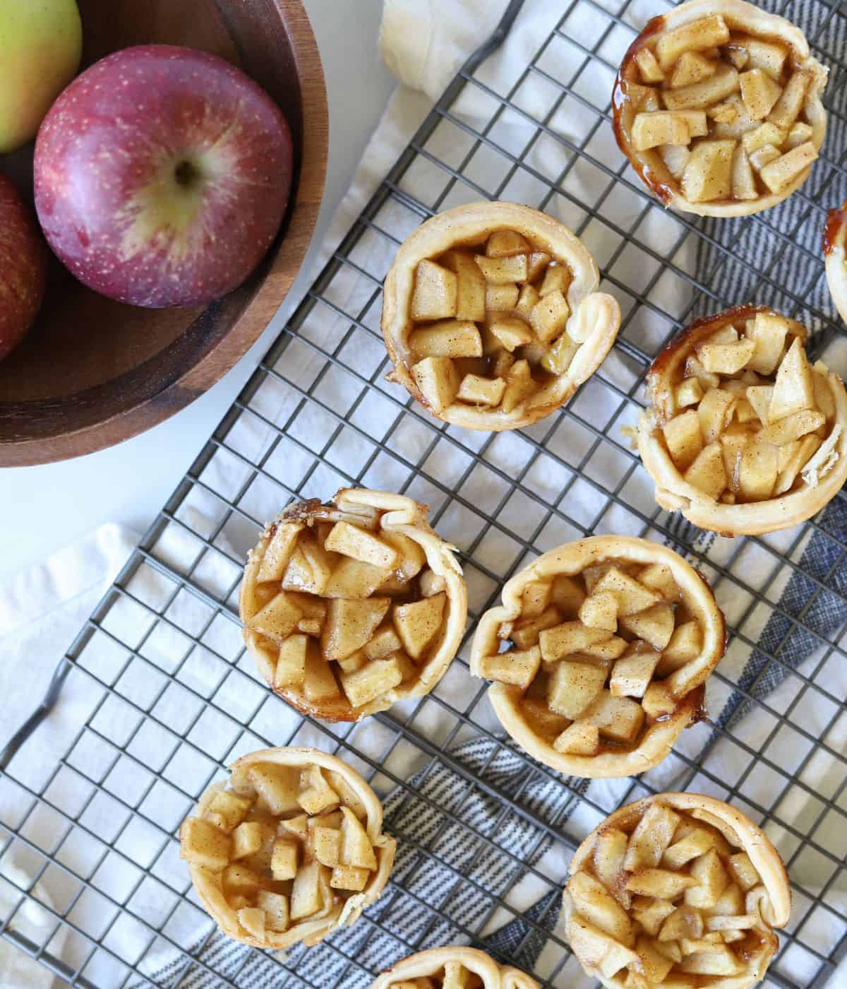 baked mini apple pies on baking rack with bowl of apples on the side