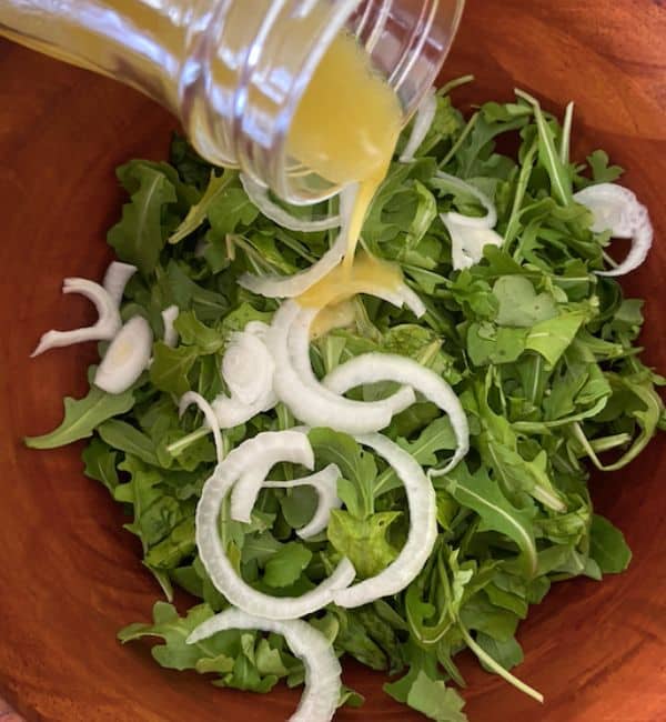 apple cider vinaigrette dressing pouring over rocket and onions