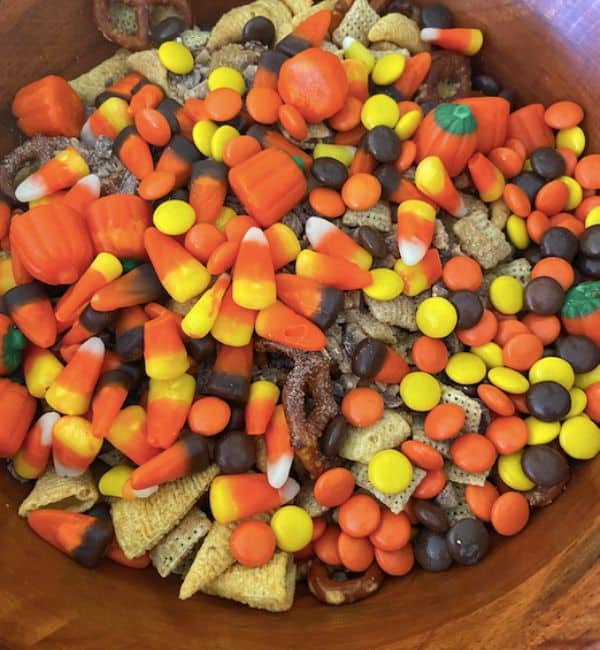 large wooden bowl full of halloween snack mix topped with candy corn, heath pieces, and reeces pieces