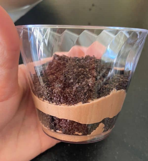 hand holding cup showing layers of pudding and cookie crumble