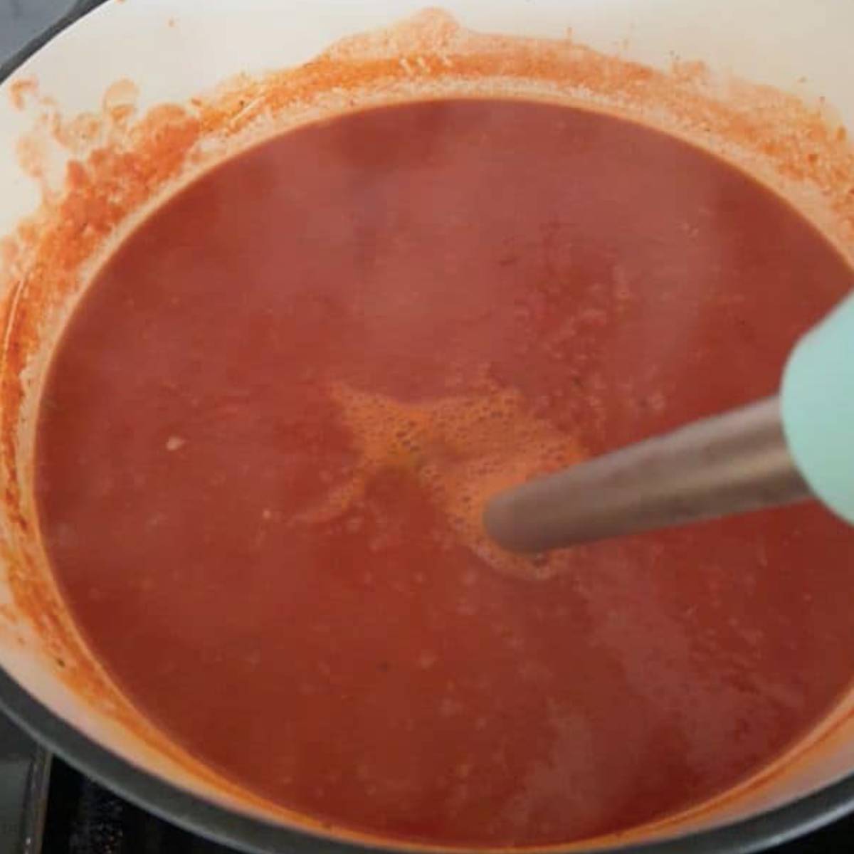 Immersion blender creating a creamy texture in tomato soup.