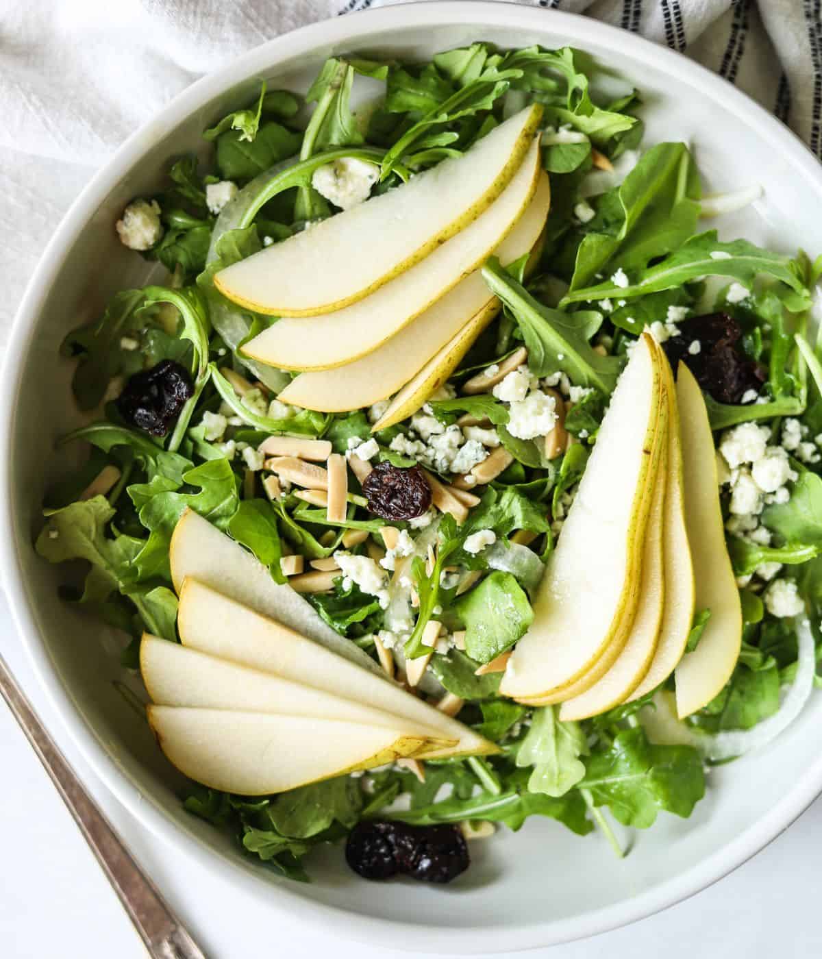 overhead view of rocket and pear salad topped with blue cheese and cherries