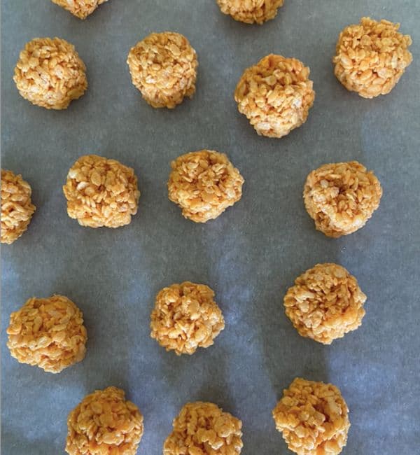 rice krispies rolled into pumpkin balls on parchment paper