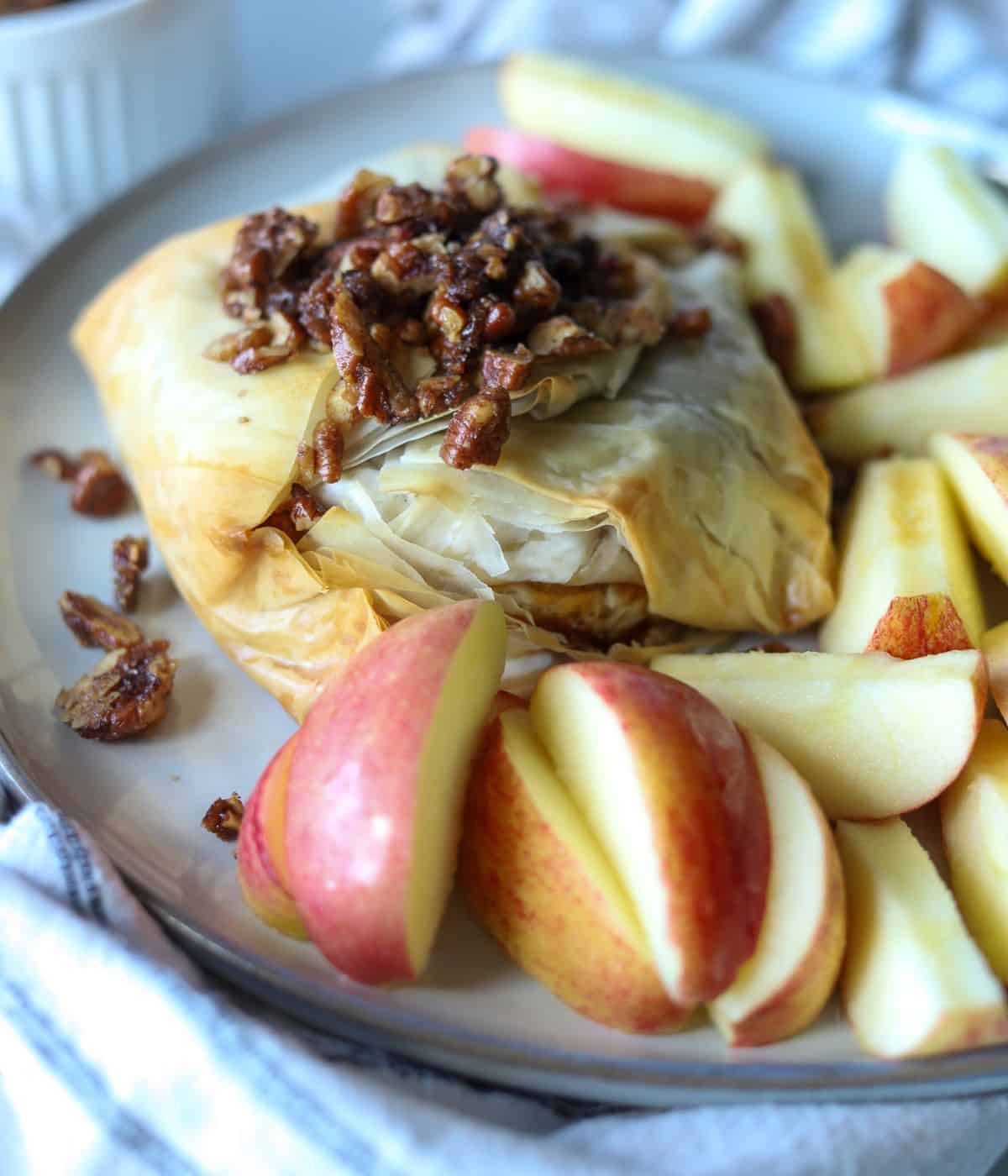 baked brie wrapped in phyllo dough with candied pecans on top with apples on the side