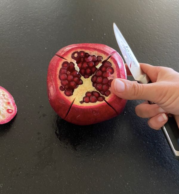 hand holding knife showing the 4 cuts down the sides of pomegranate rind