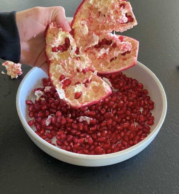 hand holding empty rind over a large bowl of pomegranate arils