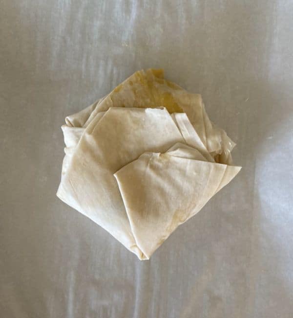phyllo dough wrapped up around the brie on parchment paper