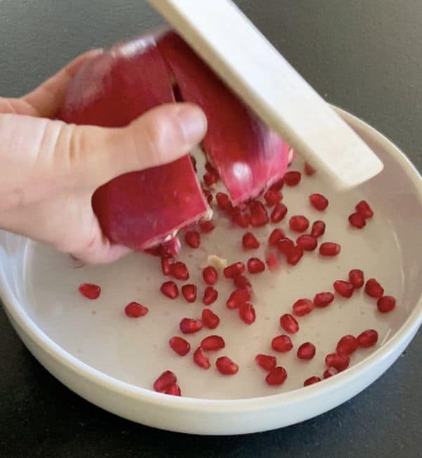 hand holding pomegranate upside down while wooden spoon hits the top